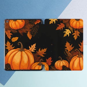 May include: A black iPad case with a fall-themed design featuring orange pumpkins and brown leaves on a black background.