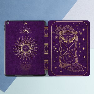 Könnte beinhalten: Violette Tabletthülle mit goldenem Sonnen-, Mond- und Stundenglas-Design. Die Hülle hat eine strukturierte, lederartige Oberfläche. Das Design umfasst himmlische Elemente und eine Motte im Stundenglas, was eine mystische Ästhetik erzeugt.