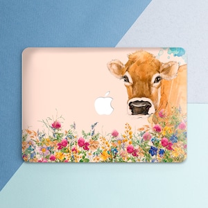 May include: A laptop skin with a watercolor illustration of a brown cow with a pink nose and white flowers. The cow is looking at the camera and has a gentle expression. The flowers are in shades of pink, yellow, and blue.