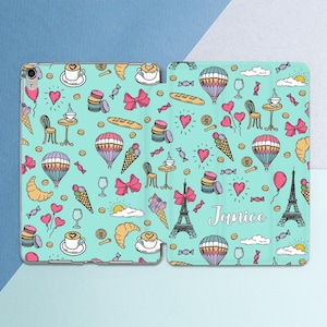 May include: A light mint green tablet case featuring a repeating pattern of hot air balloons, Eiffel Towers, croissants, macarons, ice cream cones, coffee cups, bows, and hearts. The name Janice is printed in white script on the right side.