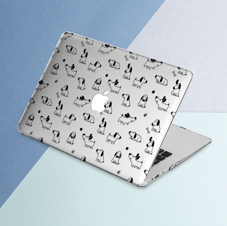 Puede incluir: Una funda transparente para port&aacute;til con un patr&oacute;n repetido de perros de dibujos animados en blanco y negro. La funda est&aacute; sobre un port&aacute;til plateado con el logotipo de Apple. El fondo es una superficie azul claro y blanca.