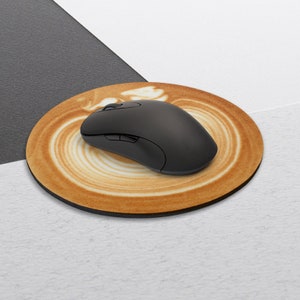 Puede incluir: Una alfombrilla de rat&oacute;n redonda de color marr&oacute;n con un dise&ntilde;o de taza de caf&eacute;. Un rat&oacute;n de ordenador negro est&aacute; encima de la alfombrilla de rat&oacute;n.