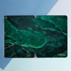 May include: An iPad case featuring a green marble effect with gold detailing. The case is open, displaying the screen and the inner cover. The name "Millie" is written in gold script on the cover. The background is a gradient of blue.