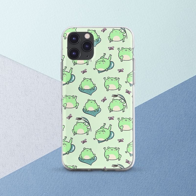 May include: A clear phone case with a green background and a repeating pattern of green frogs. The frogs are in various poses, some are sitting, some are jumping, and some are swimming. There are also small pink flowers scattered throughout the pattern.