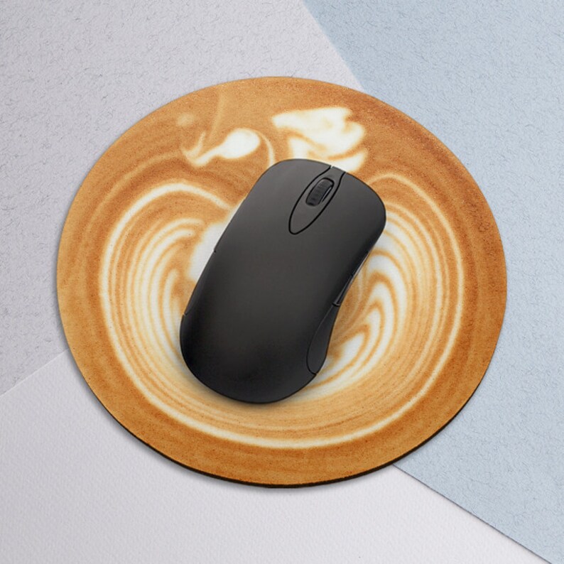 Puede incluir: Una alfombrilla de rat&oacute;n redonda de color marr&oacute;n y blanco con un dise&ntilde;o de caf&eacute; con leche. Un rat&oacute;n inal&aacute;mbrico negro est&aacute; encima de la alfombrilla de rat&oacute;n.