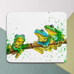 May include: Three green and blue frogs sitting on a branch with green paint splatters on a white background.