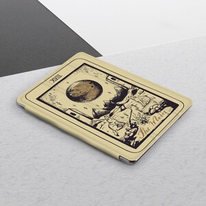 K&ouml;nnte beinhalten: Eine beige Tableth&uuml;lle mit einer Schwarzwei&szlig;illustration der Mond-Tarotkarte. Die Karte zeigt einen gro&szlig;en Mond, zwei T&uuml;rme und ein hundeartiges Wesen. Der Text "The Moon" ist in Kursivschrift am unteren Rand der Karte geschrieben.