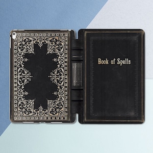 Puede incluir: Una funda para iPad de cuero negro con un diseño en relieve dorado y las palabras "Book of Spells" en la parte delantera.