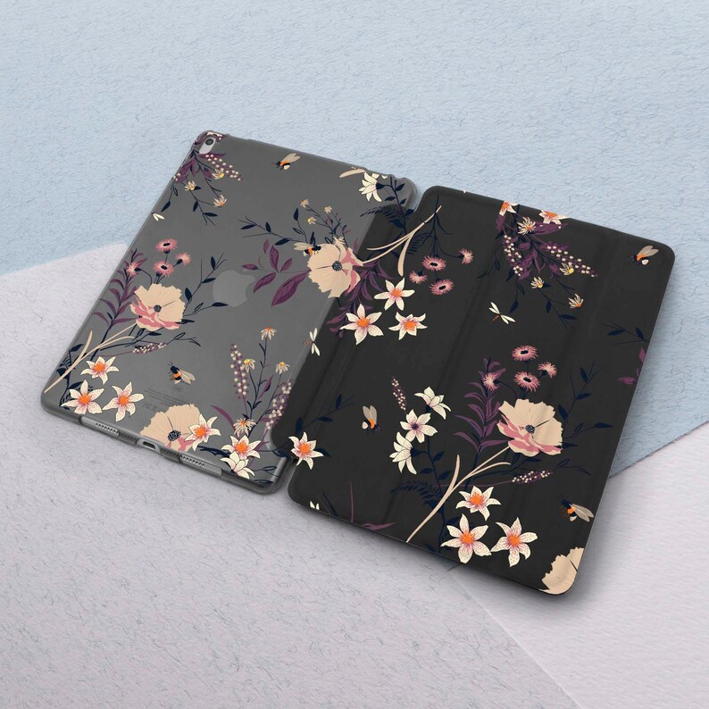 May include: Two iPad cases with floral patterns. One case is clear with a gray background and the other is black with a dark gray background. Both cases feature a floral design with pink, white, and yellow flowers.