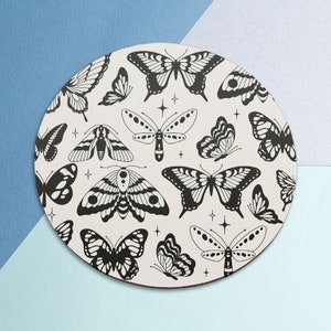 May include: A round white coaster with a black and white pattern of butterflies and moths. The design is repeated across the surface of the coaster.