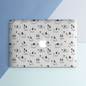 Puede incluir: Una funda para port&aacute;til con un patr&oacute;n repetido de perros, huesos y puntos negros dibujados con l&iacute;neas sobre un fondo gris claro. El logotipo de Apple es visible en el centro. El fondo es un degradado de azul claro y blanco.