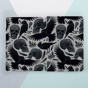 May include: A black and white phone case with a repeating pattern of skulls and ravens. The case has a matte finish and a sleek design.