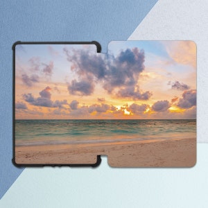May include: A scenic sunset over a calm ocean with a sandy beach in the foreground. The sky is a mix of pink, orange, and purple hues with fluffy white clouds.