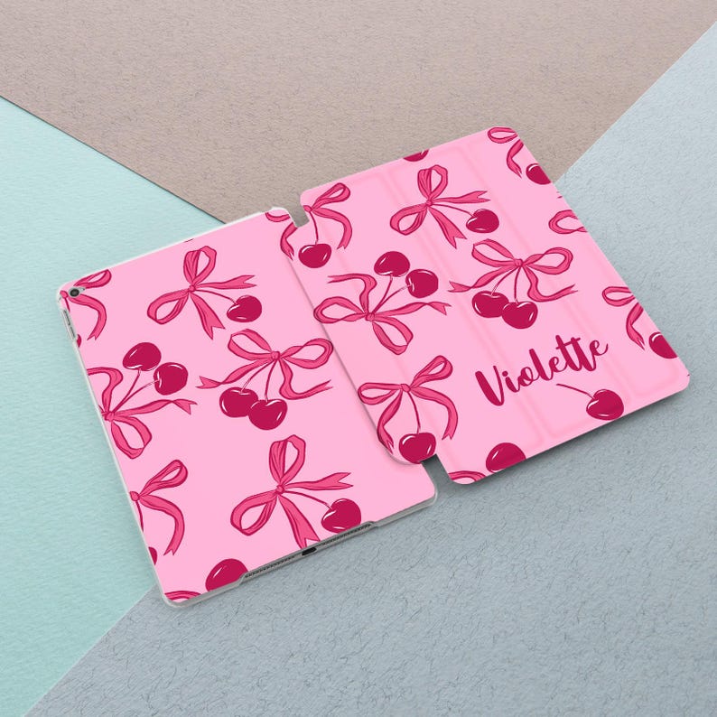 May include: Pink iPad case with a cherry and bow pattern. The case has the name "Violette" printed on the back.