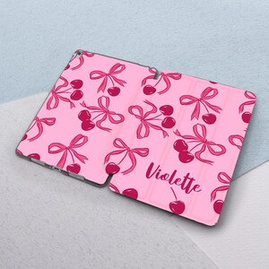 May include: Pink tablet case with a cherry and bow pattern. The case has the name "Violette" printed on it.