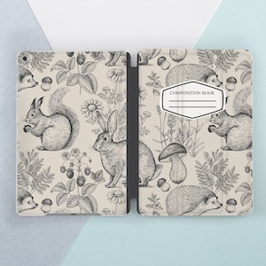 Puede incluir: Una cubierta de cuaderno de composición de color crema con una ilustración en blanco y negro de una escena de bosque. La ilustración presenta ardillas, conejos, setas y erizos. El texto "COMPOSITION BOOK" está impreso en la cubierta.