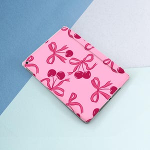 May include: Pink iPad case with a repeating pattern of red cherries and pink bows.