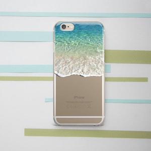 Puede incluir: Una funda transparente para teléfono con una foto de una escena de playa. La foto muestra agua azul con olas blancas rompiendo en la orilla. El texto "iPhone" está impreso en la parte posterior de la funda.