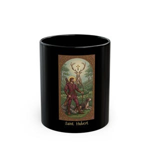 May include: Black ceramic mug featuring an illustration of Saint Hubert, a man in red attire with a bow and arrow, a dog, and a deer with a cross between its antlers. The mug has the text "Saint Hubert" at the bottom.