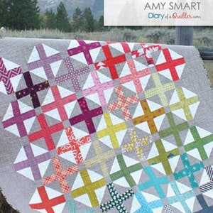 May include: A colorful quilt with a patchwork design featuring a variety of fabrics in shades of red, pink, purple, green, blue, yellow, and white. The quilt is made up of squares and triangles, and the pattern is called "Hopscotch" by Amy Smart.