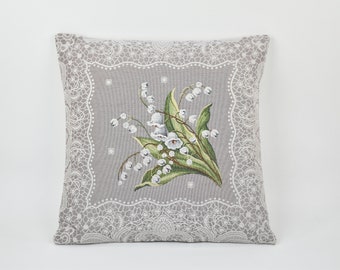 May include: A gray pillow with a white lace border and a floral design of white lilies of the valley on a gray background.