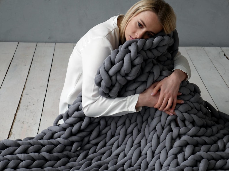 Girl is holding a weighted blanket. Handmade cotton weighted chunky knit blanket – perfect for PTSD, fibromyalgia, anxiety, ADHD, and sensory needs. It is a cotton weighted blanket - does not have glass beads. It is a handmade knit from cotton tube yarn, blanket is made by the weight that you need, from the cotton yarn amount that you need.