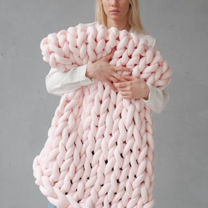Peut inclure: Une grande couverture en tricot &eacute;pais de couleur rose p&acirc;le. La couverture est faite de fil &eacute;pais et a une texture douce et moelleuse.