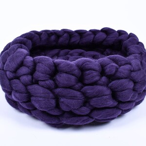 May include: A deep purple knitted pet bed made of thick yarn. The bed is round and has a deep well for a pet to curl up in.