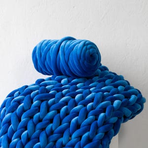 A soft, handmade chunky knit blanket crafted from plush velvet yarn, elegantly draped over a cozy couch. This giant knit throw blanket adds warmth and texture to any living space, perfect for home décor, bedding, or gifting.