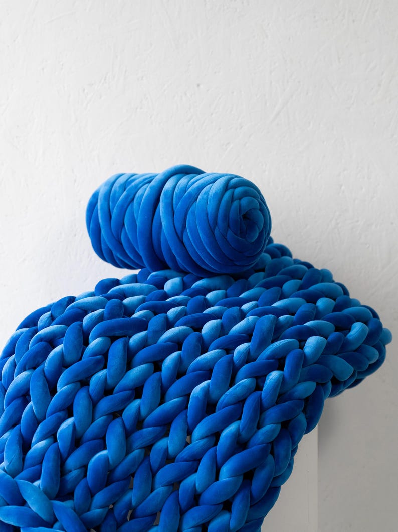 A soft, handmade chunky knit blanket crafted from plush velvet yarn, elegantly draped over a cozy couch. This giant knit throw blanket adds warmth and texture to any living space, perfect for home décor, bedding, or gifting.
