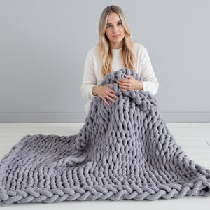 Girl on white floor holding giant grey color chenille blanket