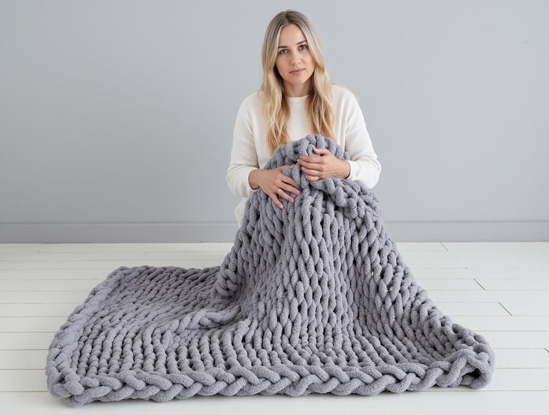 Girl on white floor holding giant grey color chenille blanket