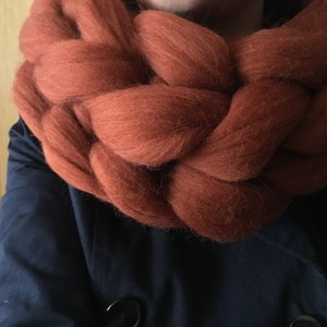 Peut inclure: Une écharpe épaisse et moelleuse en tricot de couleur orange rouille foncé. L'écharpe est faite d'un fil doux et duveteux et est tressée en une forme épaisse de corde.