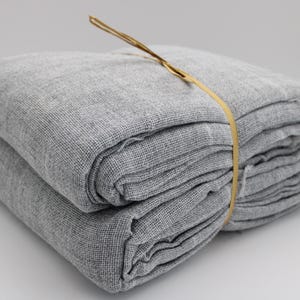 May include: A folded stack of gray linen fabric, bound with a thin, light brown twine. The fabric has a textured weave and appears soft. The bundle is neatly arranged, suggesting it is ready for use. The overall aesthetic is simple and natural.
