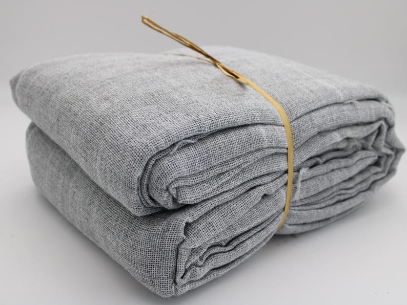 May include: A folded stack of gray linen fabric, bound with a thin, light brown twine. The fabric has a textured weave and appears soft. The bundle is neatly arranged, suggesting it is ready for use. The overall aesthetic is simple and natural.