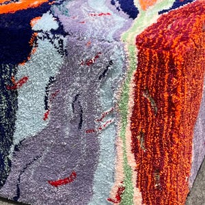 May include: A colorful, textured cube with a variety of colors including orange, navy blue, light blue, purple, and red. The cube appears to be made of a soft, plush material, possibly fabric or yarn.