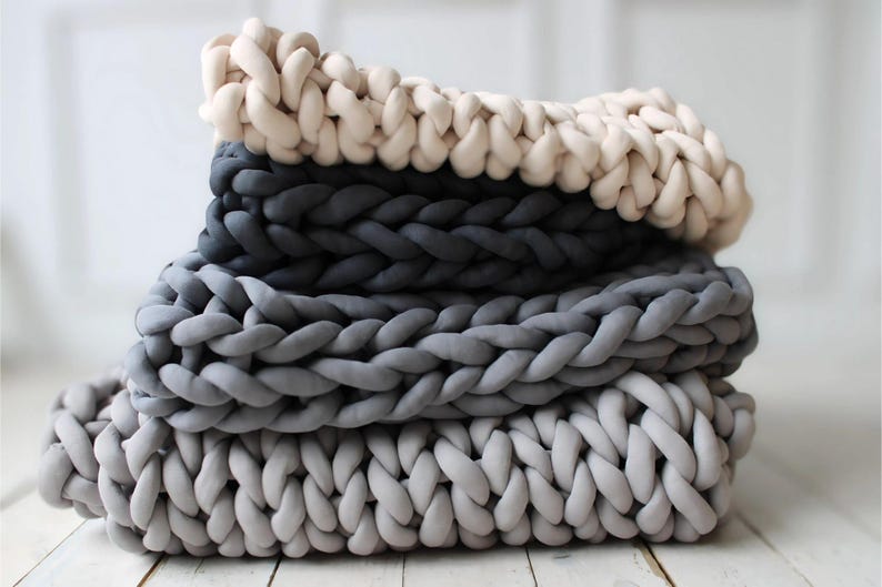 Peut inclure: Une pile de quatre couvertures en tricot &eacute;pais dans des tons de gris et de blanc. Les couvertures sont faites de fil &eacute;pais et doux et ont un aspect confortable et textur&eacute;.