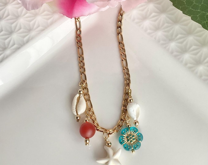 Un collier  délicat en chaîne dorée, orné de charms marins : coquillages, étoile de mer, perle colorée et fleur turquoise.