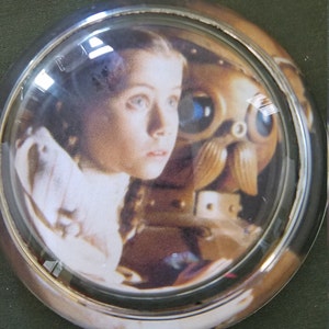 May include: A glass dome paperweight with a printed image of a young girl and a robot from the movie A.I. Artificial Intelligence.