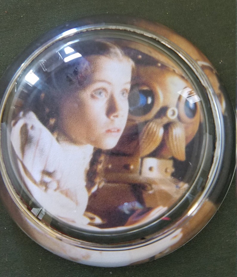 May include: A glass dome paperweight with a printed image of a young girl and a robot from the movie A.I. Artificial Intelligence.