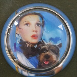 May include: A blue and silver car steering wheel knob with a picture of Dorothy from the Wizard of Oz and her dog Toto.