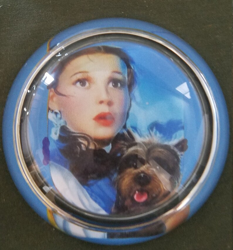 May include: A blue and silver car steering wheel knob with a picture of Dorothy from the Wizard of Oz and her dog Toto.