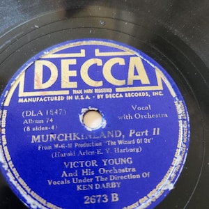 May include: Vintage vinyl record with a blue and gold label. The label reads "DECCA" and features the title "MUNCHKINLAND, Part II" from "The Wizard of Oz." The record is by Victor Young and his Orchestra, with vocals directed by Ken Darby.