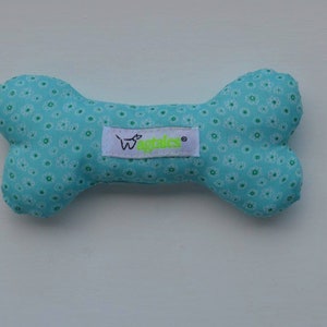 May include: A light blue dog bone toy with a white and green floral pattern. The toy has a white label with the text "Wagtails" in green.