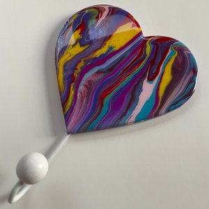 May include: A white heart-shaped hook with a colorful abstract design. The hook is made of resin and has a white metal hanger.