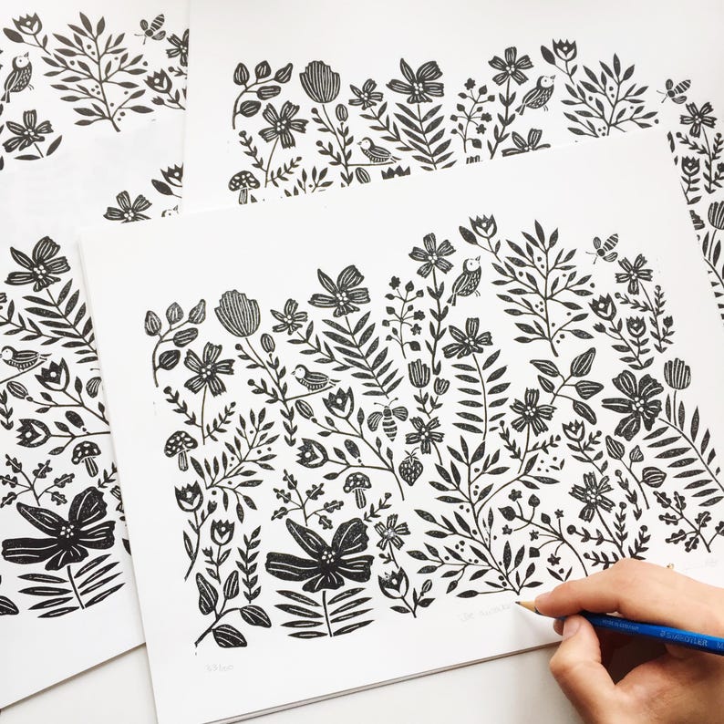May include: Black and white print of a floral design with birds, bees, and mushrooms. The print is on white paper and is being drawn on with a pencil.