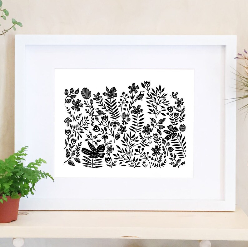 May include: Black and white print of a floral design with birds, butterflies, and mushrooms. The print is framed in a white frame.
