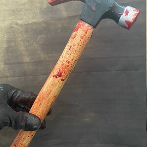 May include: A wooden-handled hammer with a black metal head, splattered with red paint to look like blood.