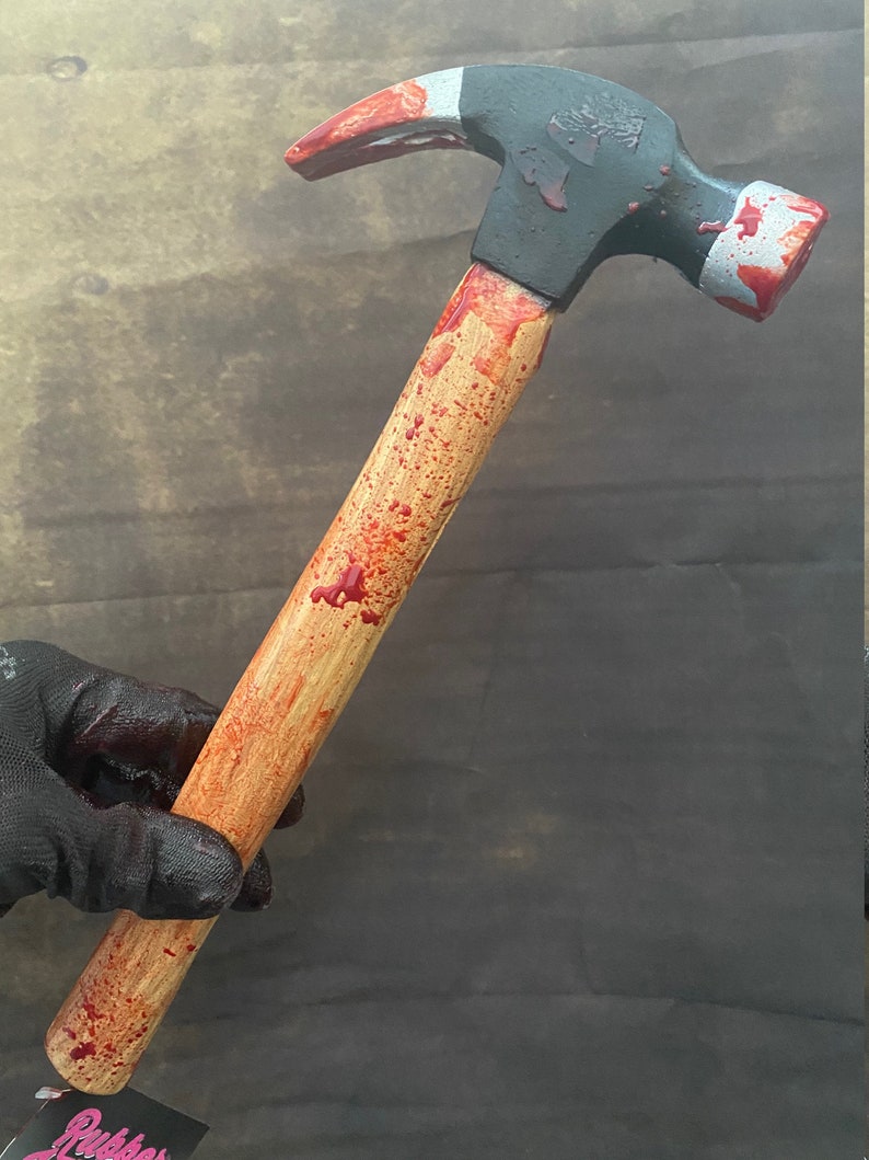 May include: A wooden-handled hammer with a black metal head, splattered with red paint to look like blood.