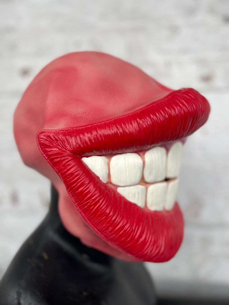 Puede incluir: Una m&aacute;scara de goma roja con una gran sonrisa exagerada. La m&aacute;scara tiene dientes blancos y labios rojos.